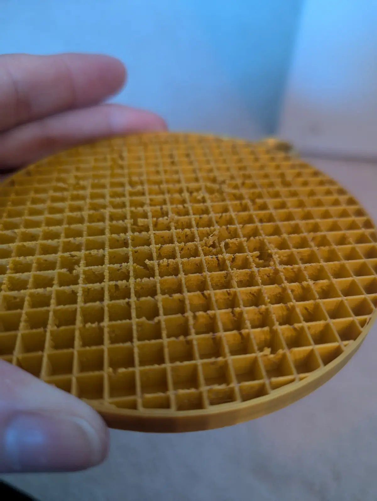 A close-up photo shows a person's hand holding a round, golden-brown waffle with a grid pattern. The waffle has visible bite…