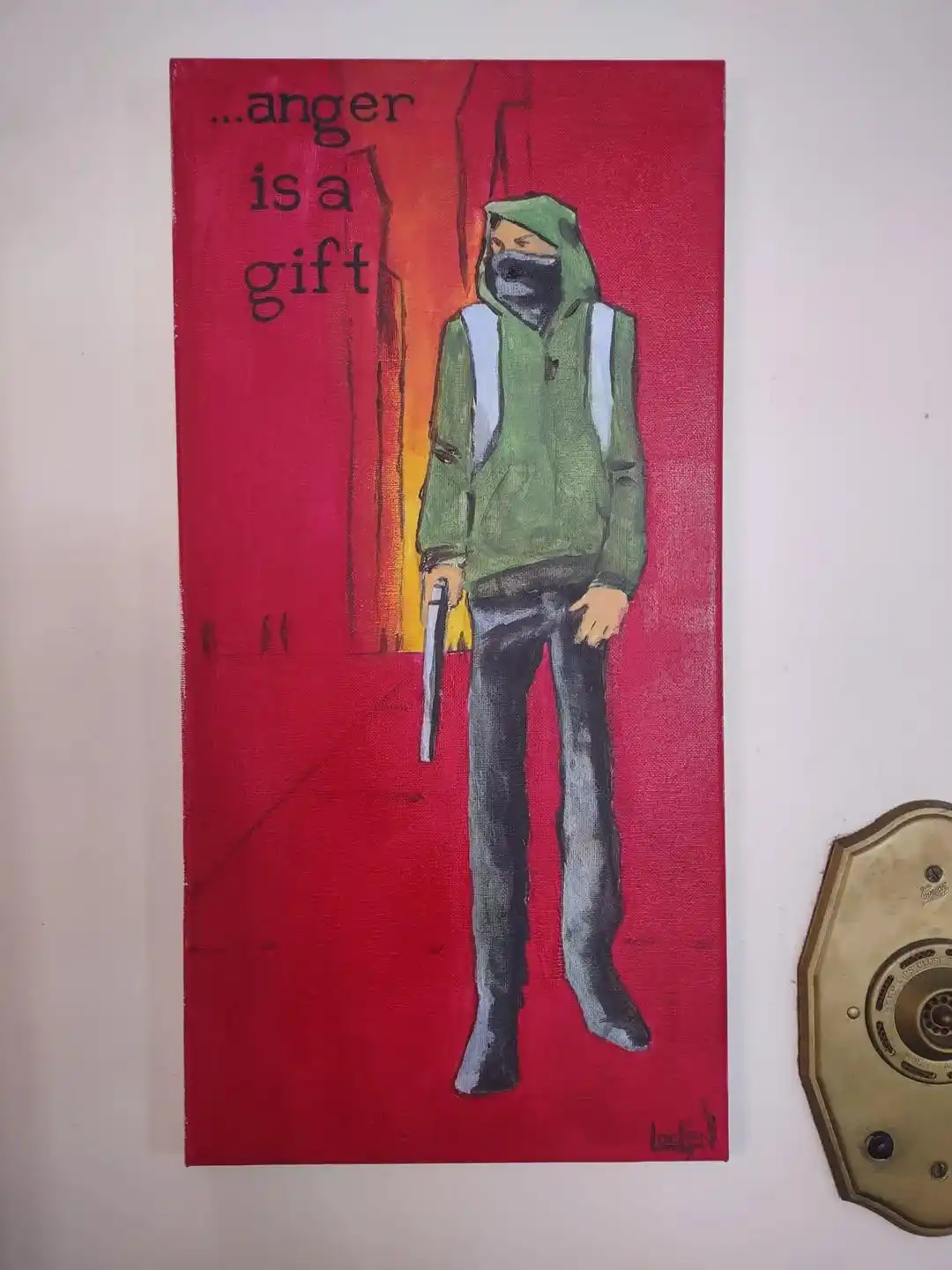 A painting depicts a hooded, masked figure in a green hoodie and dark pants holding a knife, standing against a red…