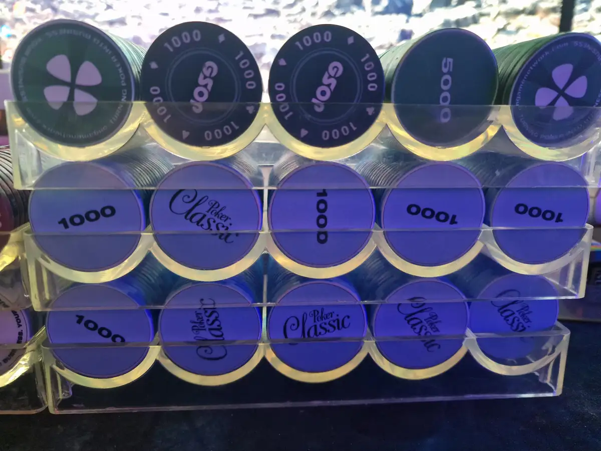 Stacks of poker chips in a clear acrylic holder show various denominations, including green 1000 and 5000 chips and blue…