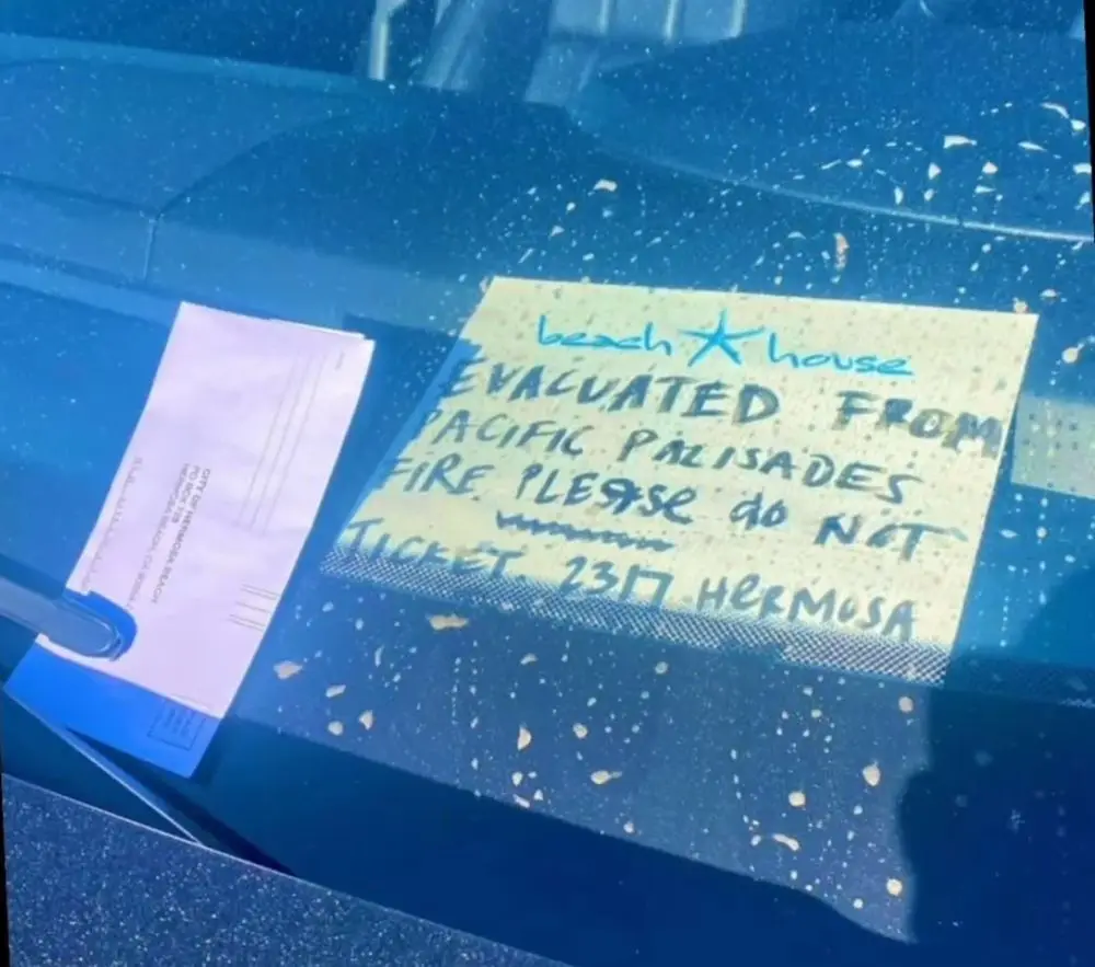 A handwritten note on a yellow sticky note is taped to a car's windshield, which is speckled with dirt or debris. The note…