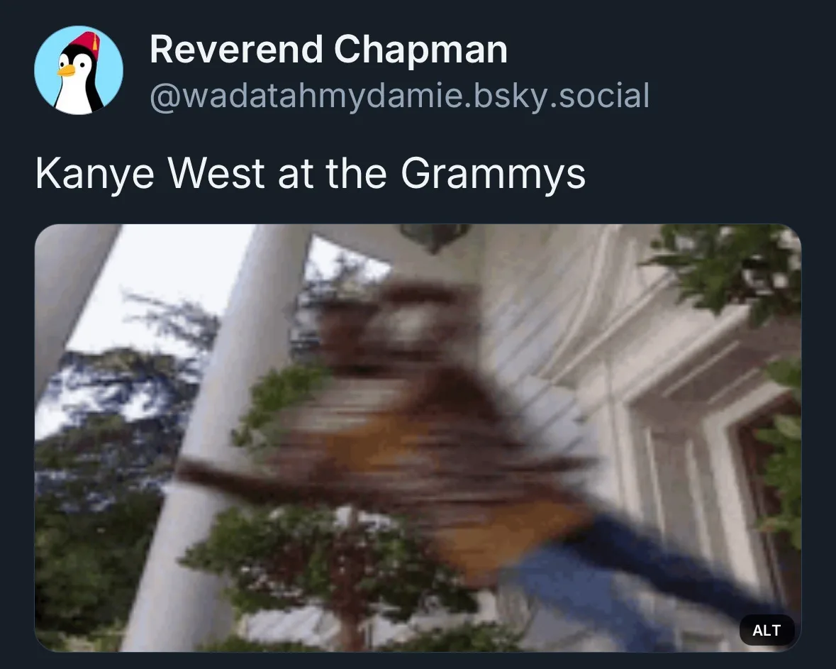 A heavily motion-blurred image of a person in a brown jacket and blue pants moving quickly in front of a white building with…