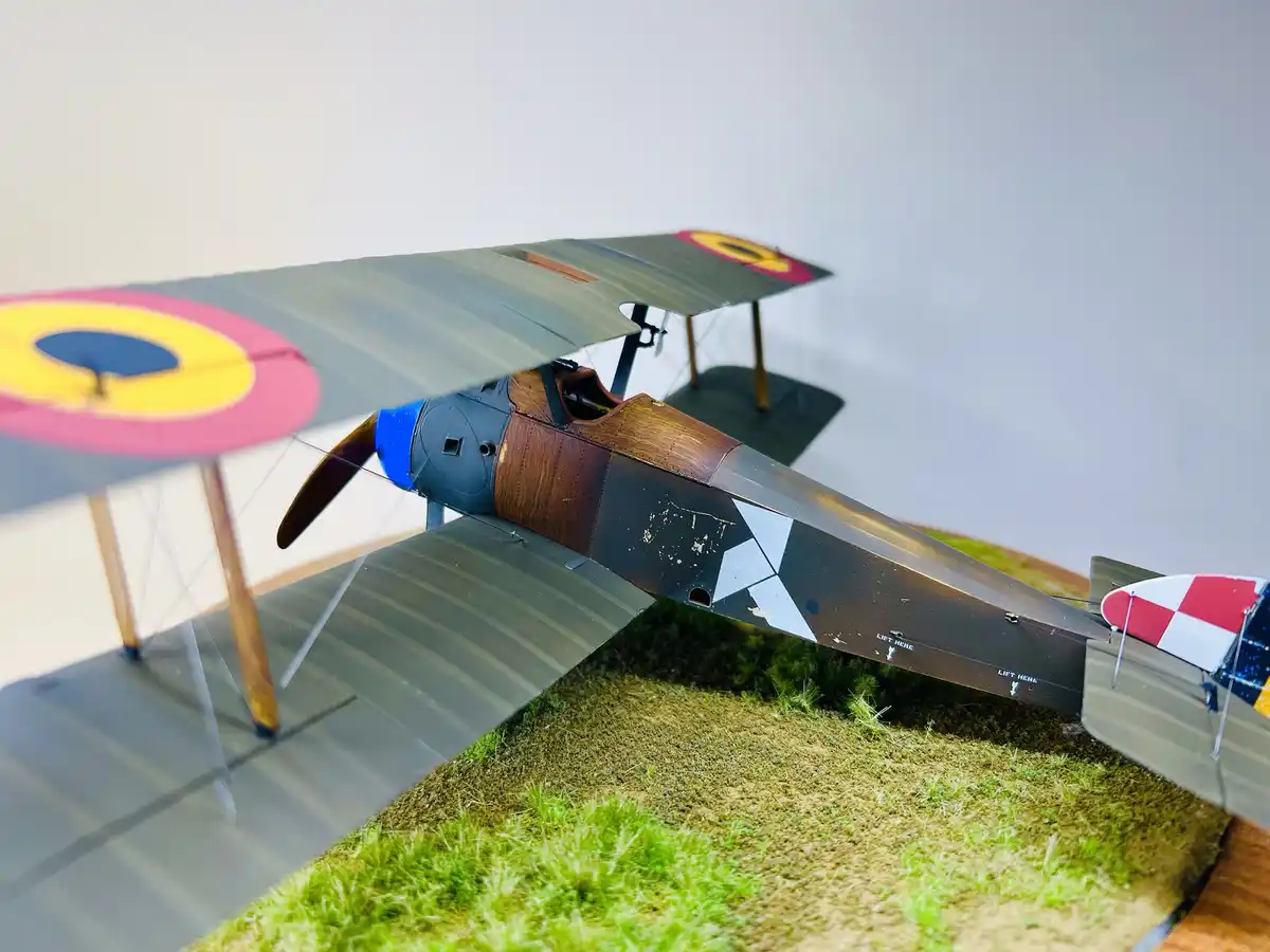 A detailed model of a vintage biplane with colorful roundels on its wings and a red-and-white checkered tail, resting on a…