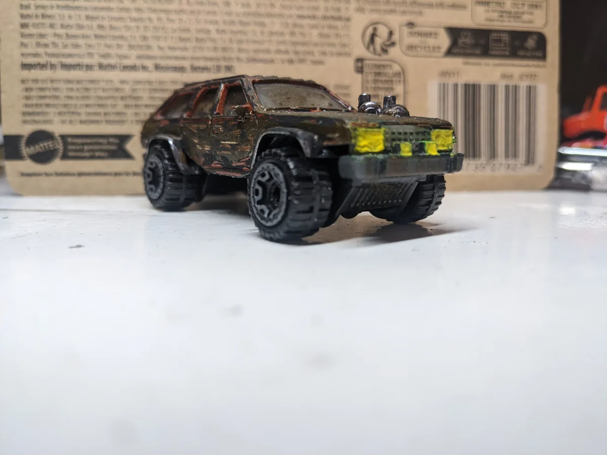 A heavily weathered and customized toy car, resembling a rugged off-road vehicle with chipped paint, large tires, and yellow…