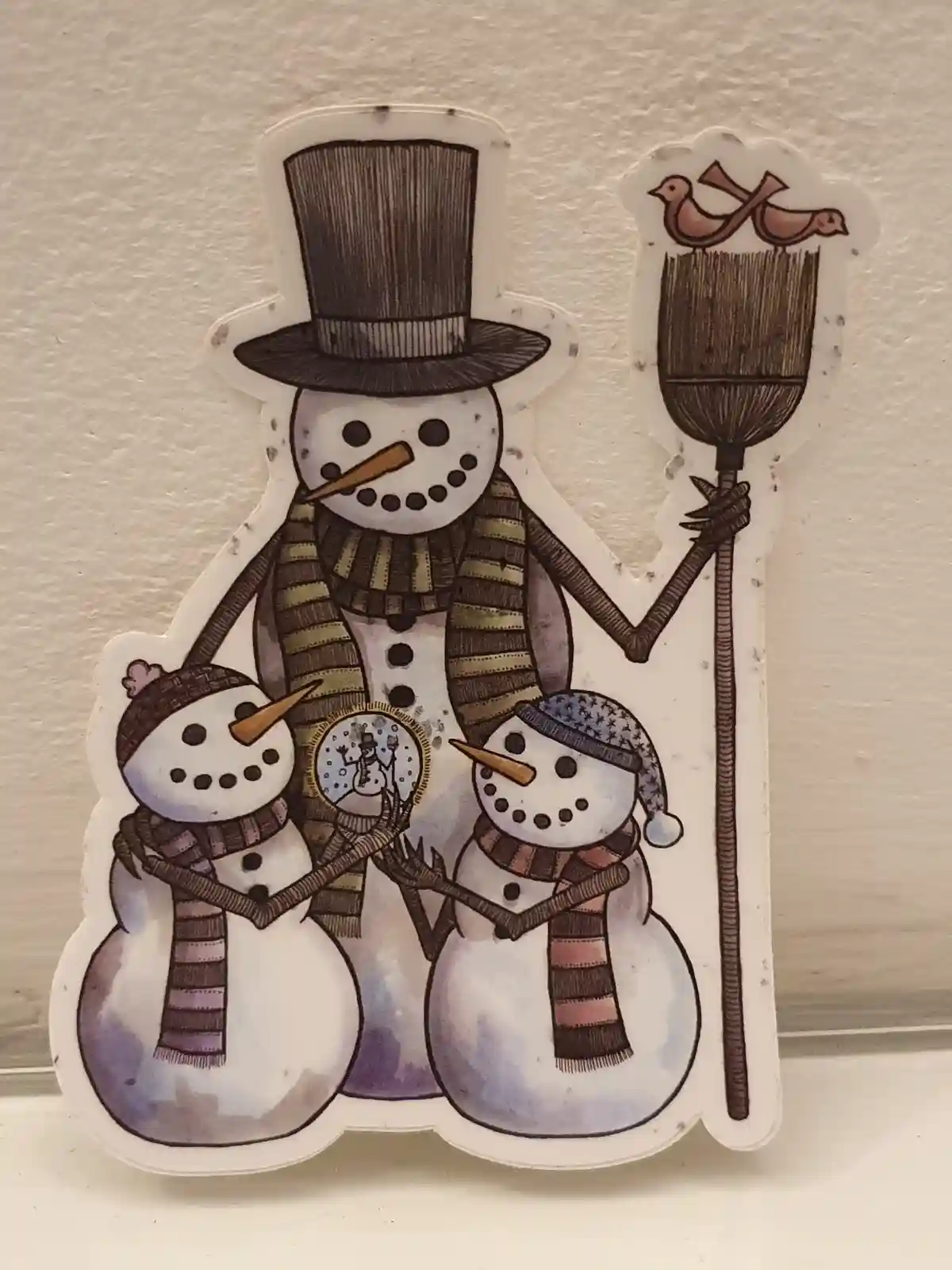 A decorative sticker shows a family of three snowmen: a tall one wearing a top hat and holding a broom with two birds…