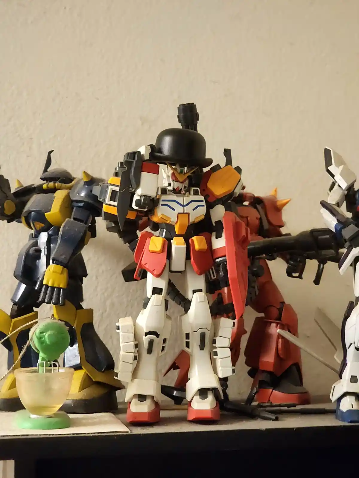 A white, red, and orange robot model wearing a black bowler hat stands among other robot models on a shelf. To its left, a…