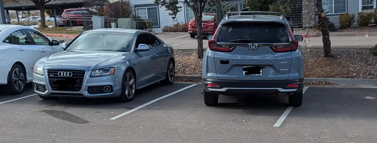 A silver Audi A5 coupe is parked next to a silver Honda CR-V in a parking lot, with the Honda's rear license plate and a…
