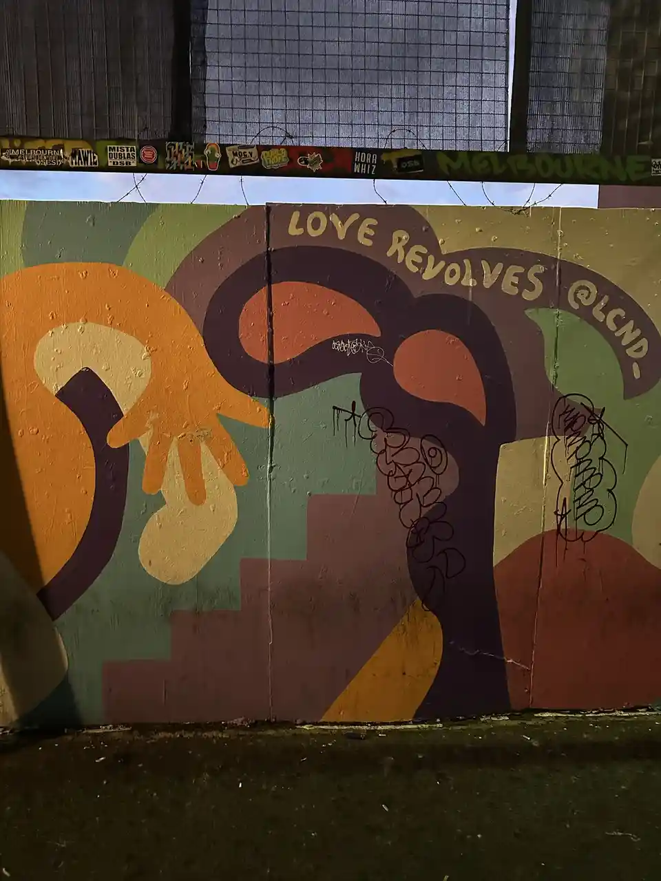 A colorful mural on a concrete wall depicts two abstract, stylized hands reaching toward each other, with the text 'LOVE…
