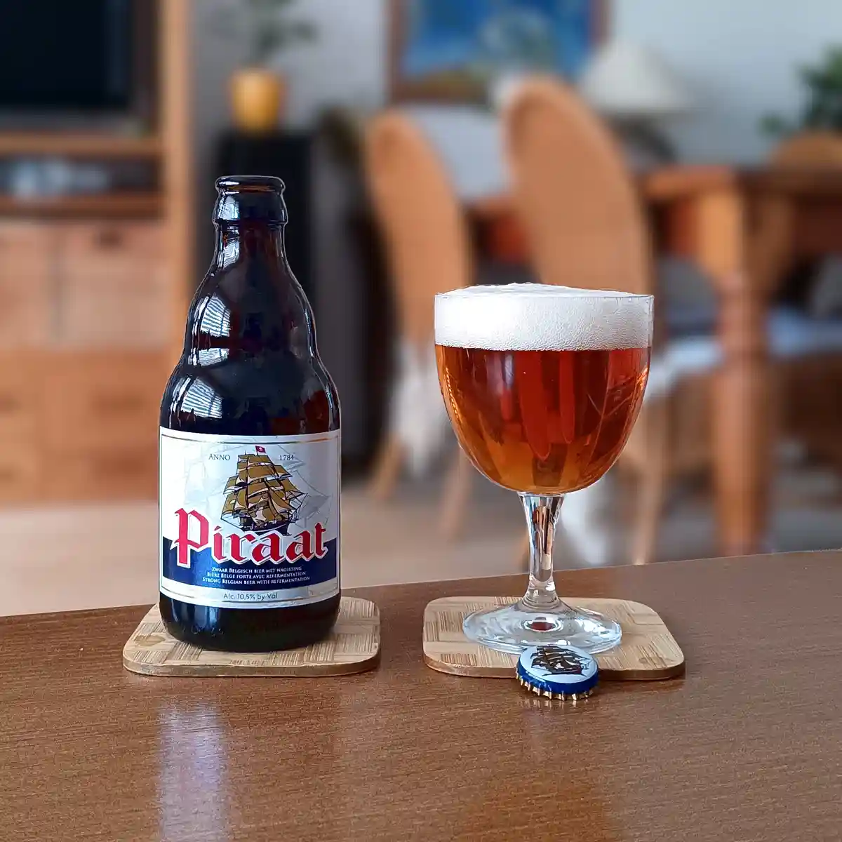 A dark brown bottle of Piraat beer with a label featuring a ship and red text sits next to a stemmed glass filled with amber…
