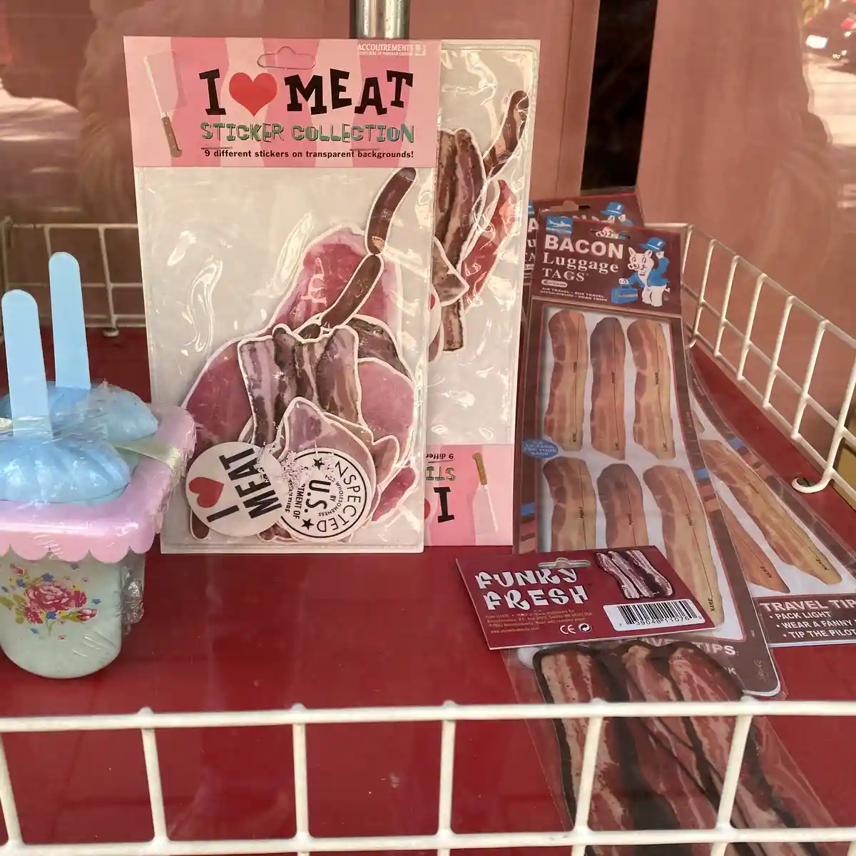 A retail display features novelty meat-themed merchandise, including a 'I ❤️ MEAT STICKER COLLECTION' package with various…