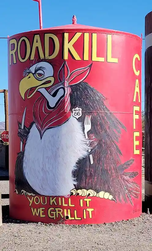A red cylindrical tank painted with a cartoon eagle wearing a red bandana, holding a knife and fork, with a Route 66 shield…