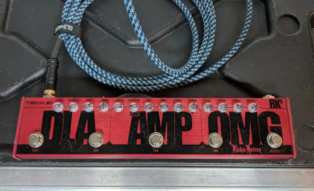 A red Tech 21 guitar effects pedal labeled 'DIAL AMP OMG' with multiple knobs and footswitches, resting on a black textured…
