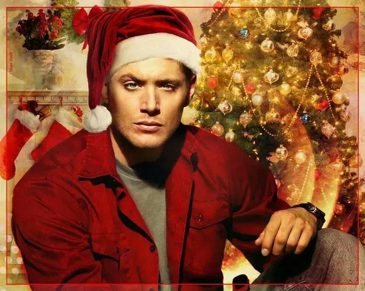 a man wearing a red santa hat and red jacket sits in front of a decorated christmas tree with stockings and ornaments, with…