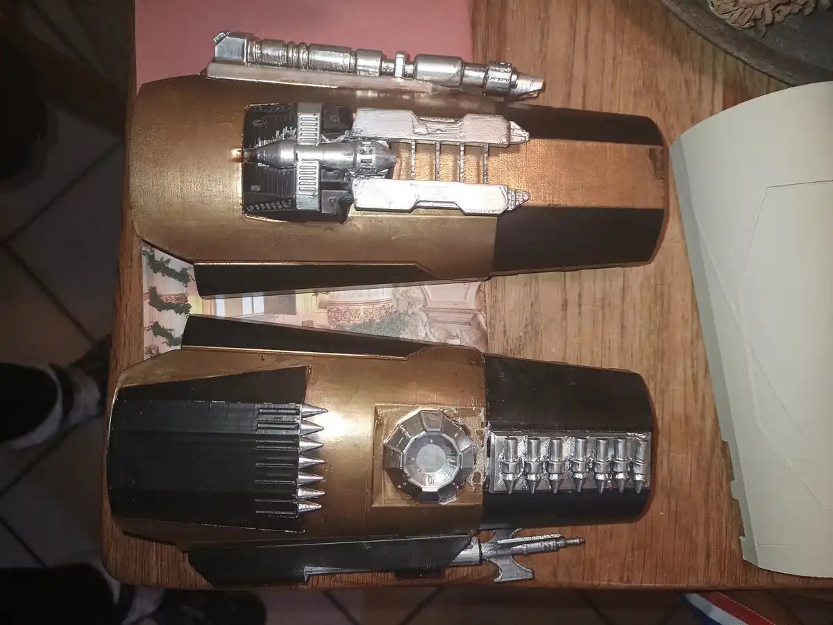 Two homemade, sci-fi style gun props made from pens and other small metal parts are displayed on a wooden table. The top…