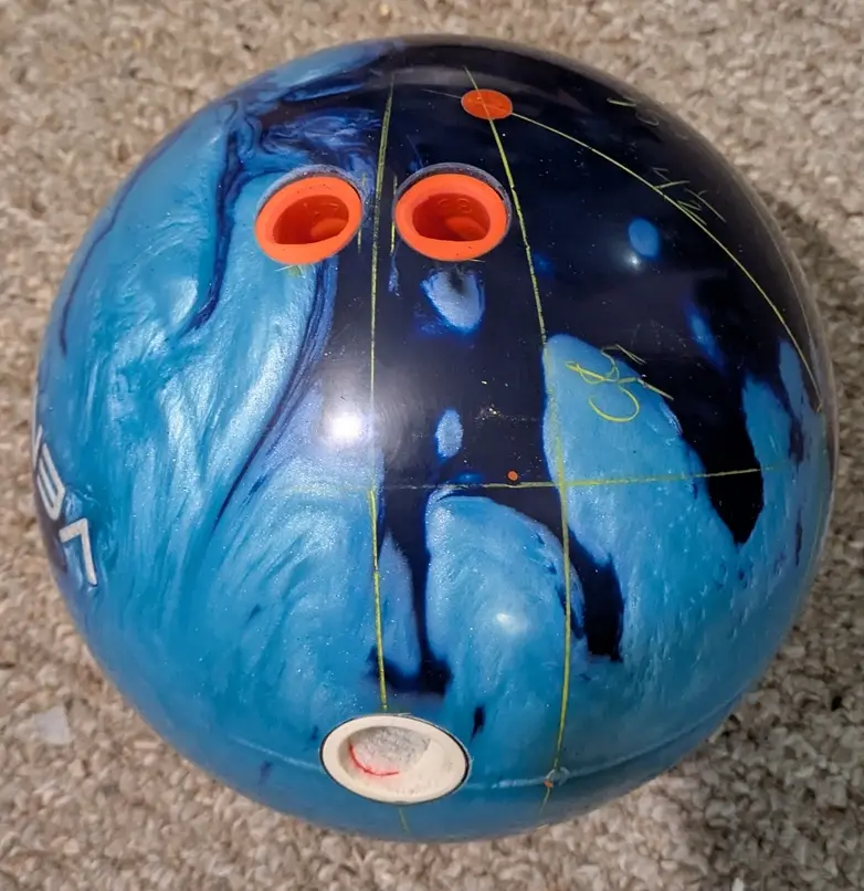A close-up photo of a blue and black marbled bowling ball with three finger holes and a thumb hole, overlaid with yellow…