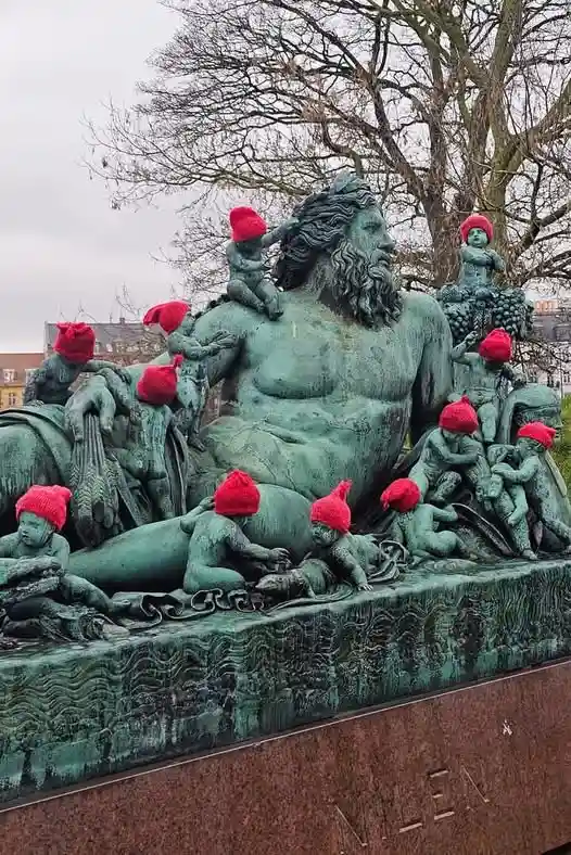 a large bronze statue of the sea god neptune, surrounded by smaller figures, has red knit hats placed on the heads of all…