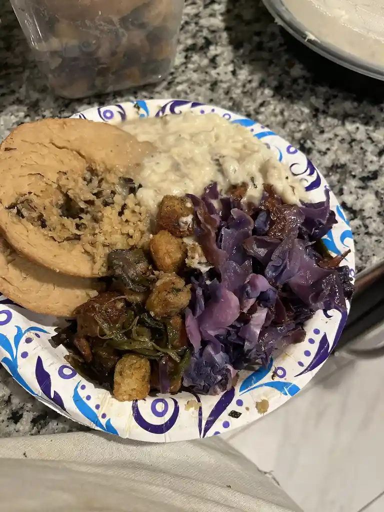 A close-up photo shows a paper plate with a variety of foods including a half-eaten bagel, creamy mashed potatoes, purple…