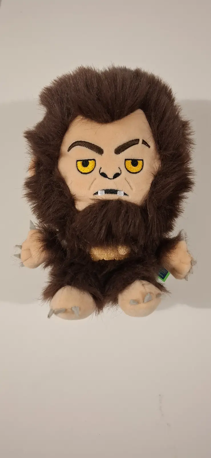 A plush toy of a furry, angry-looking beast with yellow eyes, brown fur, and claws, sitting against a plain background. The…