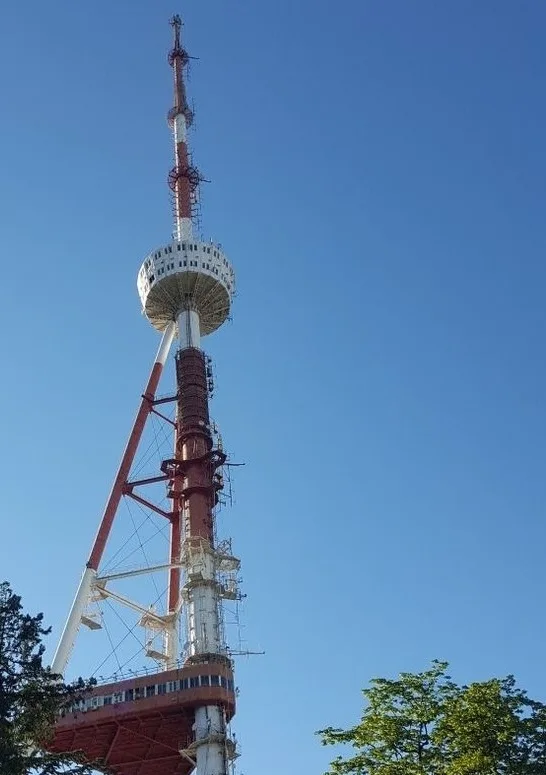 A tall red and white telecommunications tower with a circular observation deck and antenna array stands against a clear blue…