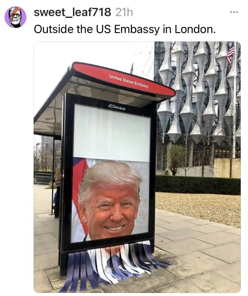 A photo shows a bus shelter outside the US Embassy in London, with a large digital screen displaying a smiling portrait of…