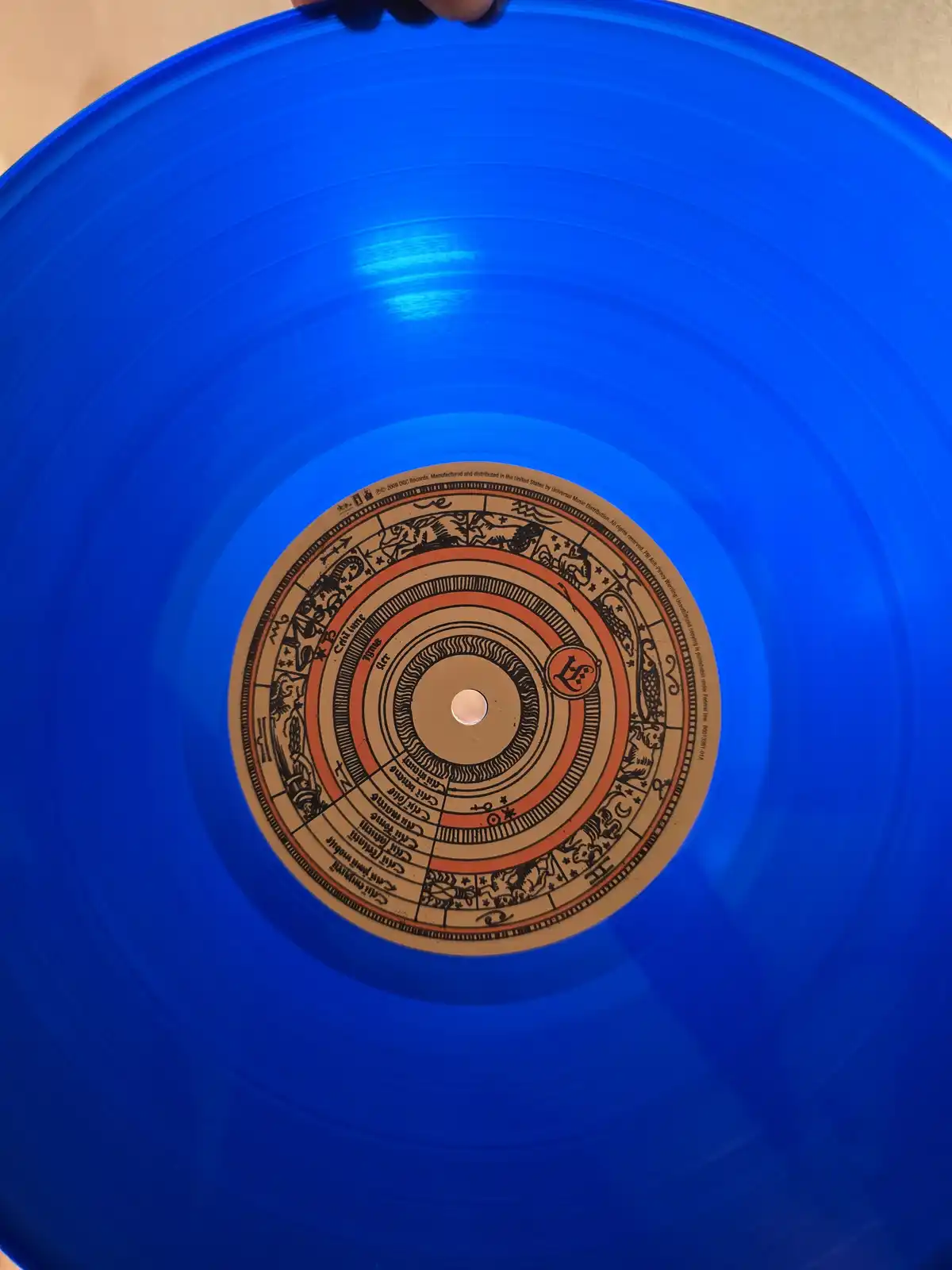 A close-up photo shows a bright blue vinyl record being held by a hand at the top edge. The record's center label features a…