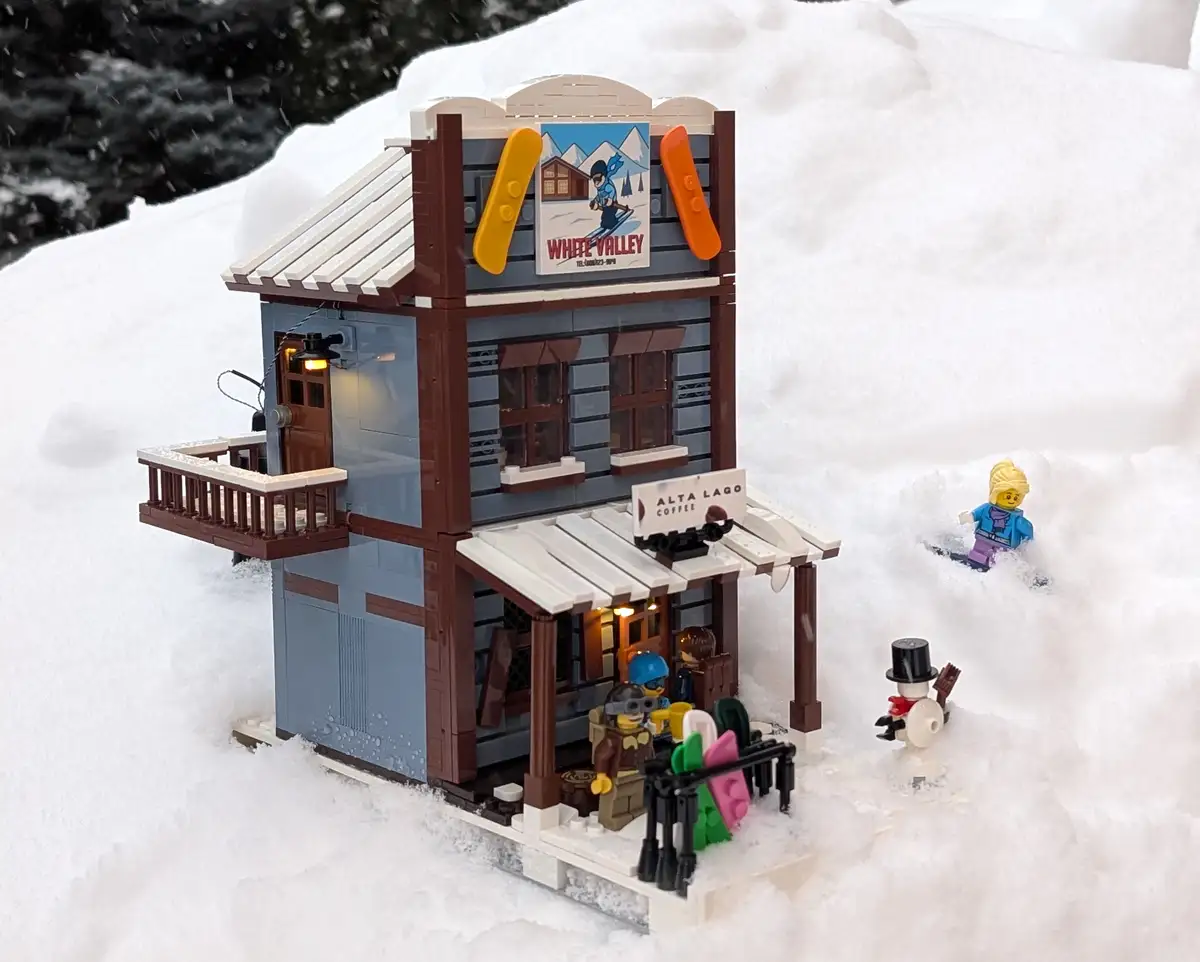 A LEGO model of a two-story ski lodge with a sign reading 'WHITE VALLEY' and 'ALTA LAGO COFFEE', set in a real snowy outdoor…