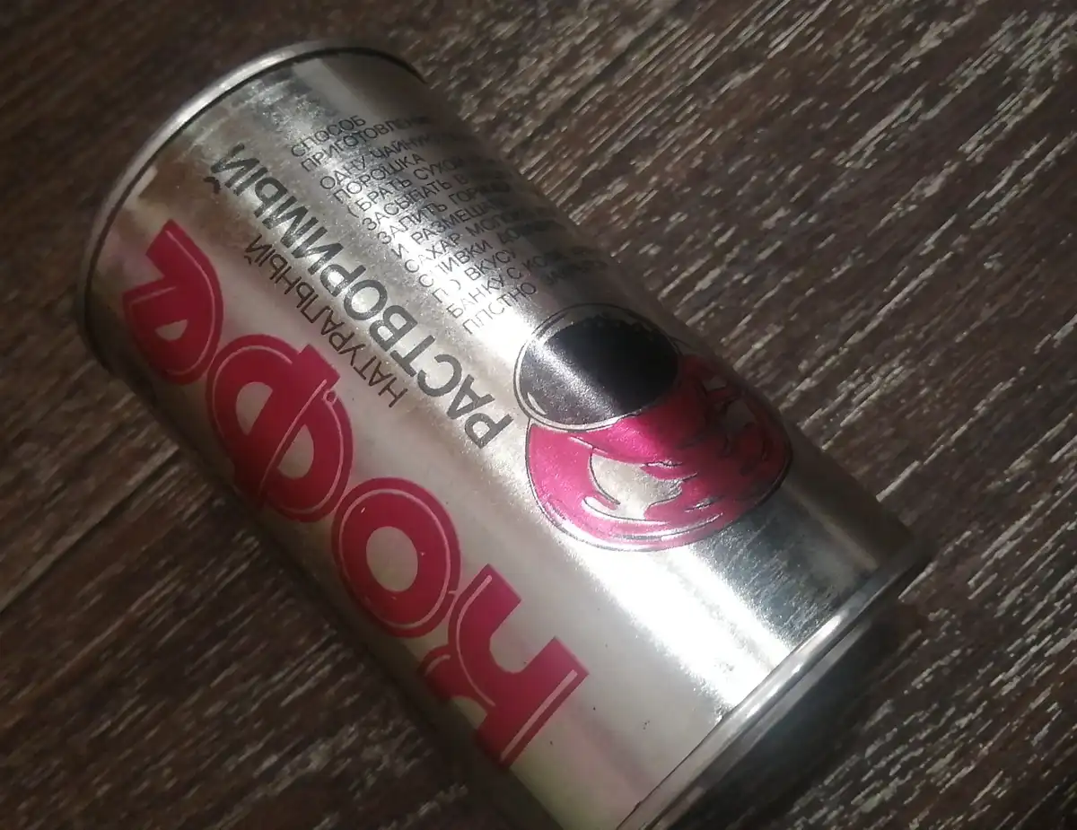 A close-up photo of a silver canister labeled 'Напиток' (Drink) in large red Cyrillic letters, lying on a dark wooden…