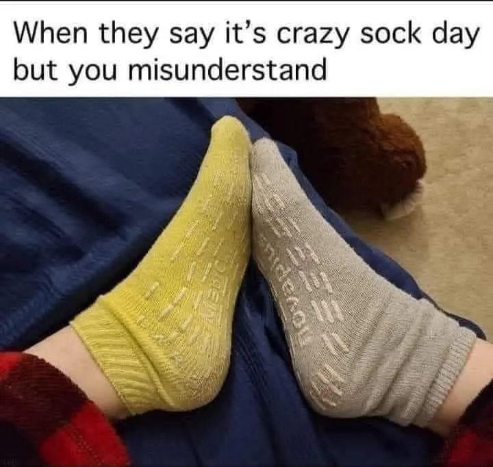 A close-up photo shows two mismatched socks, one yellow and one beige, both with visible text patterns, worn on feet resting…
