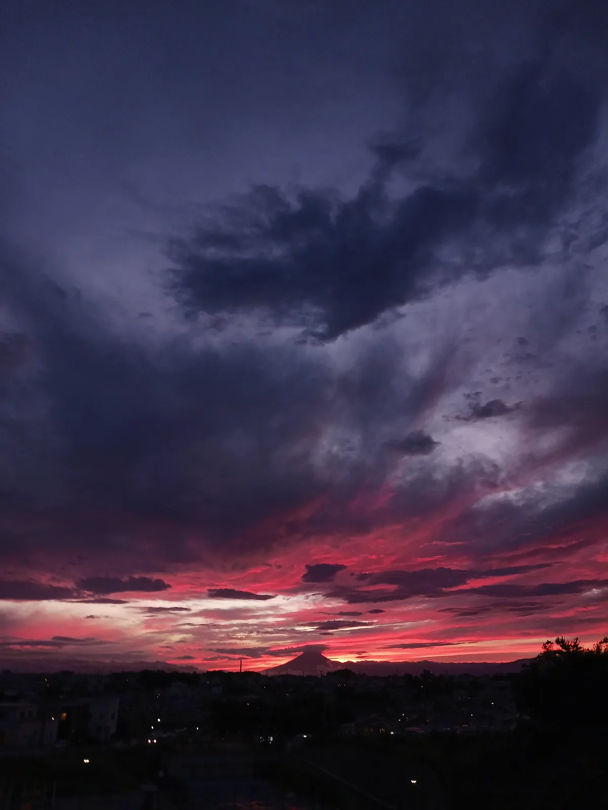 A dramatic sunset photograph shows Mount Fuji silhouetted against a sky filled with deep purple and fiery red clouds, with a…