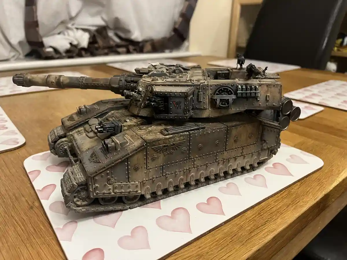A heavily detailed, weathered, and painted miniature tank model, resembling a Warhammer 40k vehicle, sits on a white…
