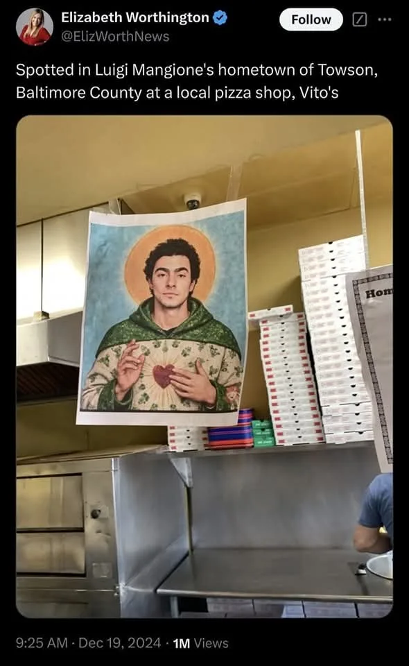 A poster in a pizza shop kitchen depicts a man with dark hair and a halo, wearing a green robe and holding a heart, styled…