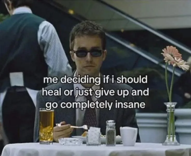 A man in a suit and sunglasses sits at a restaurant table, holding a spoon over food, with a glass of beer, salt, pepper…