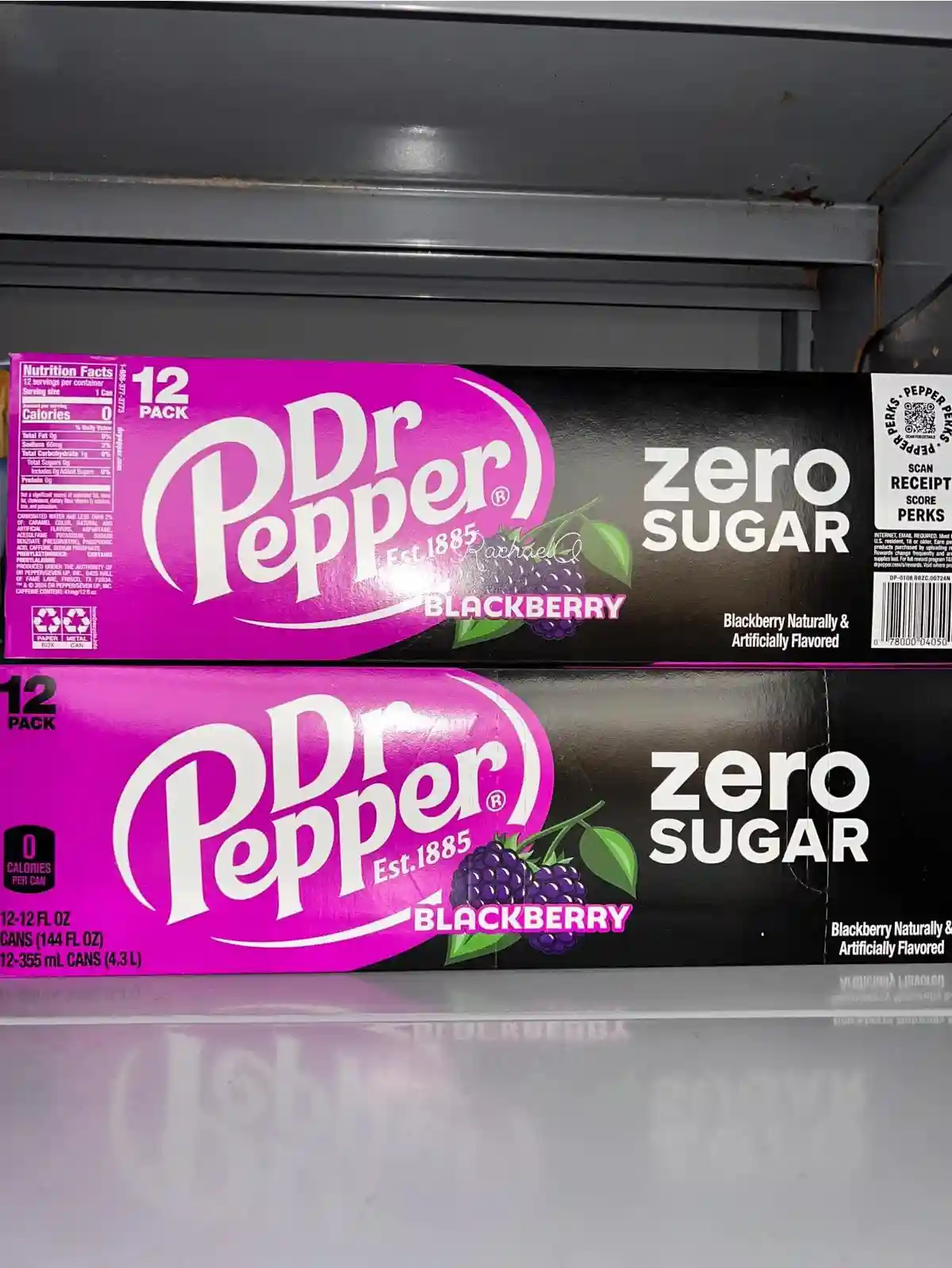 Two identical 12-pack boxes of Dr Pepper Blackberry Zero Sugar sit on a store shelf, one slightly above the other. The…