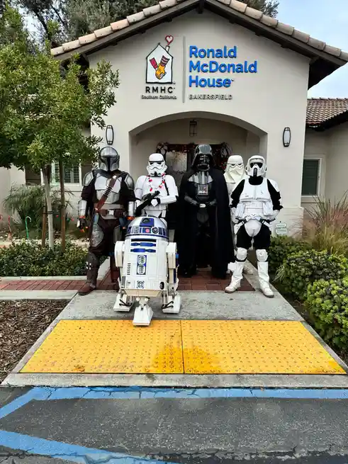 A group of people dressed as Star Wars characters — including Darth Vader, Stormtroopers, The Mandalorian, and R2-D2 — pose…