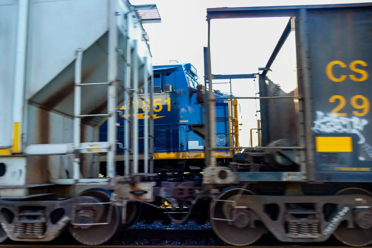 A motion-blurred photograph of a blue freight train with visible locomotive number 851 and a dark freight car marked 'CS…