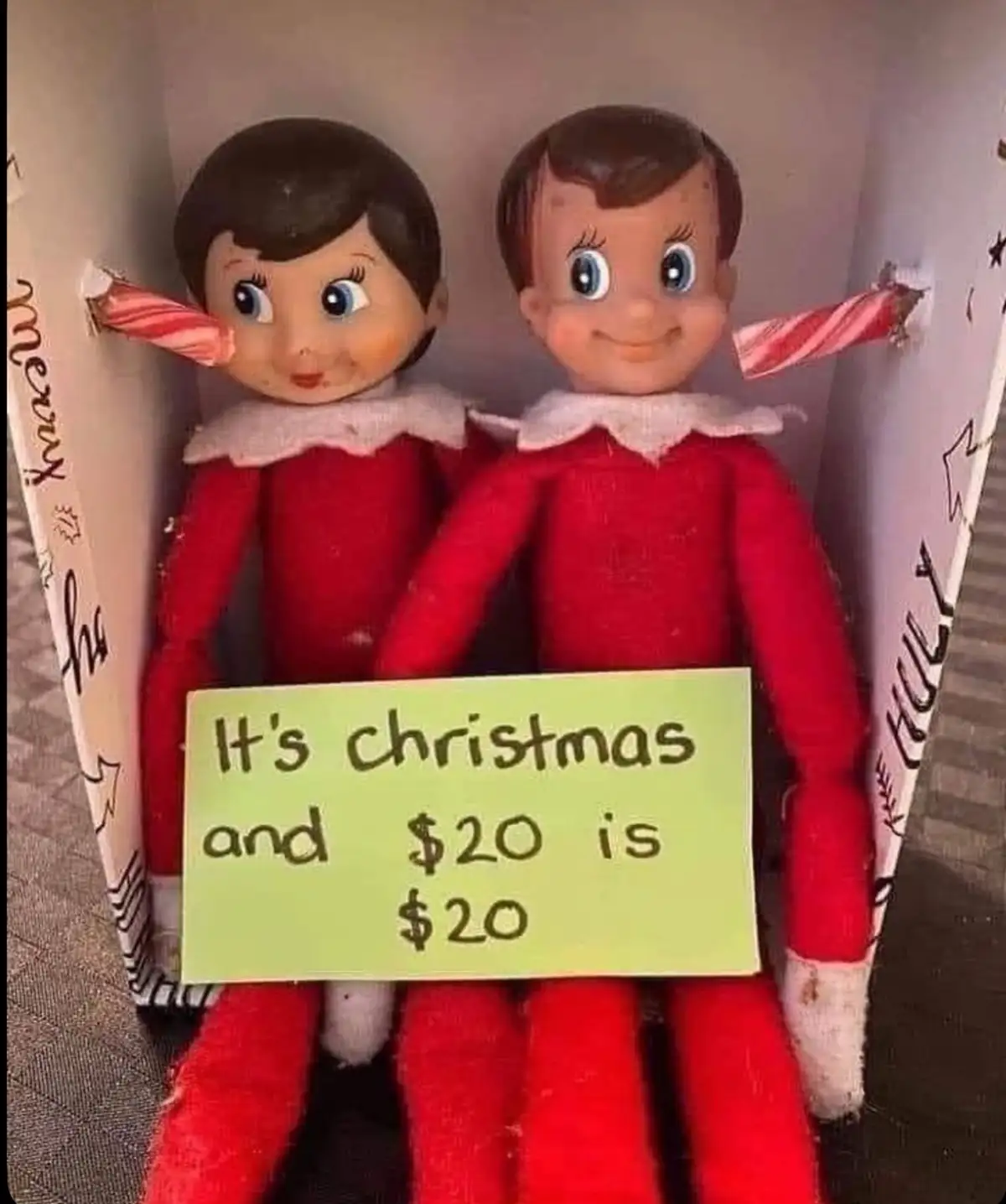 Two classic red-clothed elf dolls with candy cane sticks protruding from their ears sit side-by-side in a decorated…