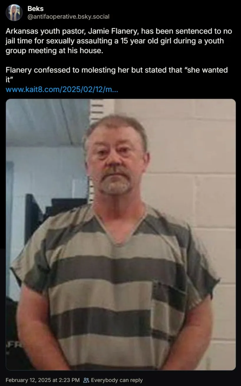 A mugshot of a middle-aged man with a mustache wearing a striped prison jumpsuit, standing in front of a white cinder block…