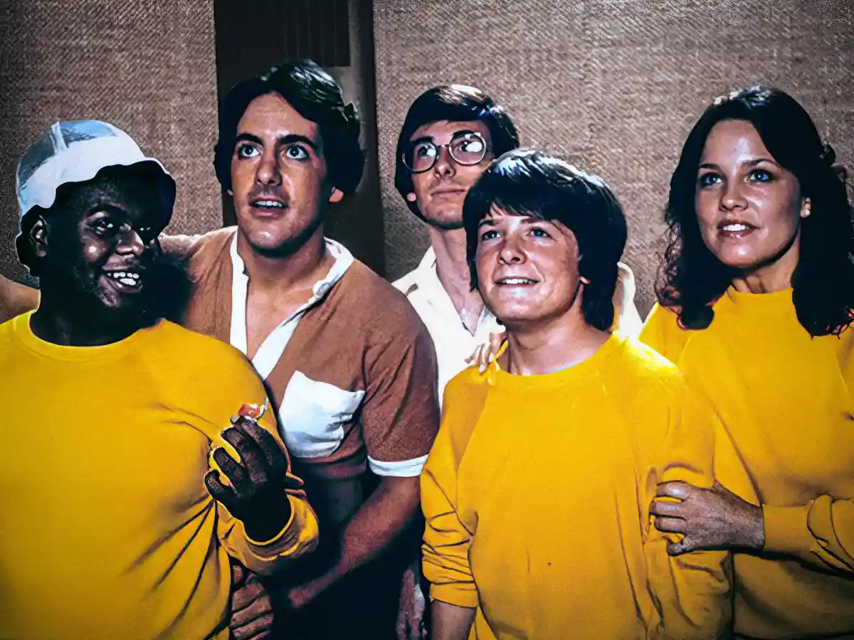 Five people, including a man in a white cap and yellow shirt holding a hot dog, are shown with shocked or surprised…