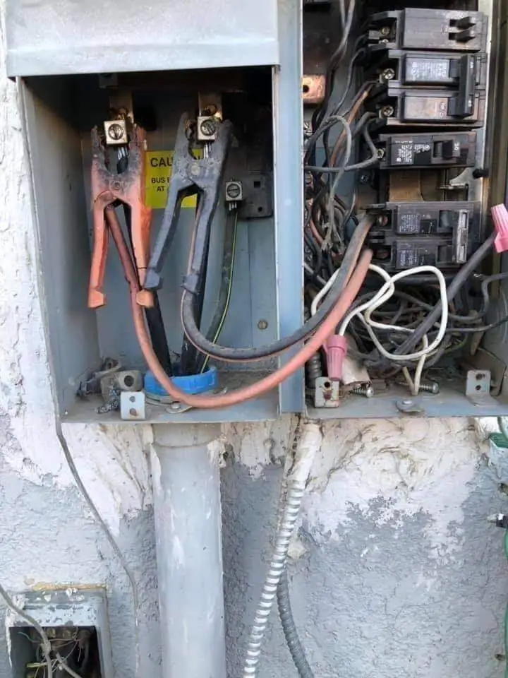 An open electrical panel with exposed wires and circuit breakers, featuring a pair of large, rusty bolt cutters plugged into…