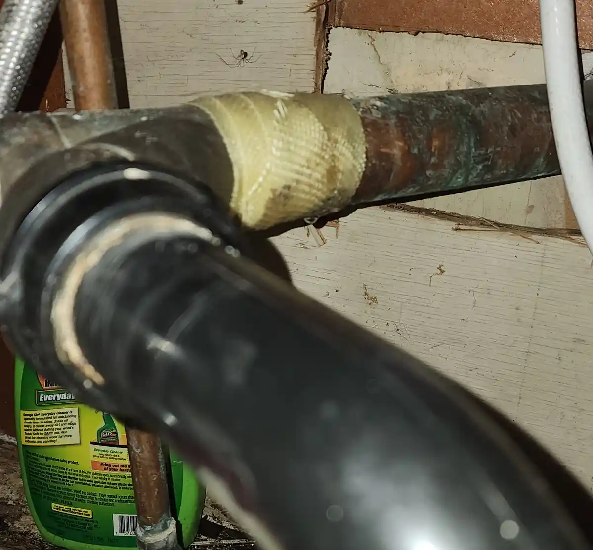 A close-up photo shows a copper pipe with a yellowish woven tape wrap, set against weathered wood walls. A green bottle of…