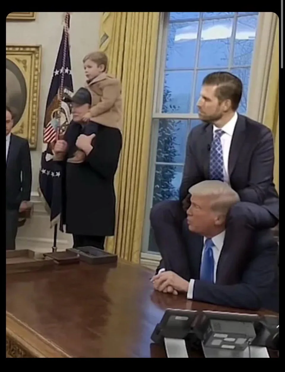 In the Oval Office, a man sits at a large wooden desk with his head resting on his hands. Behind him, another man in a suit…