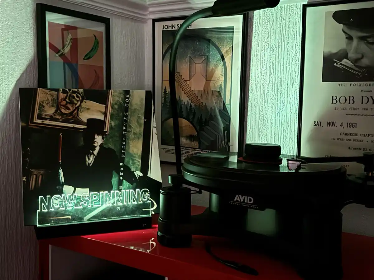 A vinyl record player sits on a red table with a Bob Dylan album cover prominently displayed, glowing with the text 'NOW…