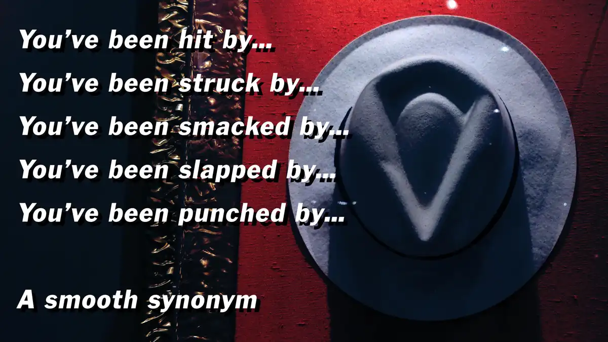 The image shows a close-up of a dark gray fedora hat resting on a red textured surface, with a metallic, wavy object…