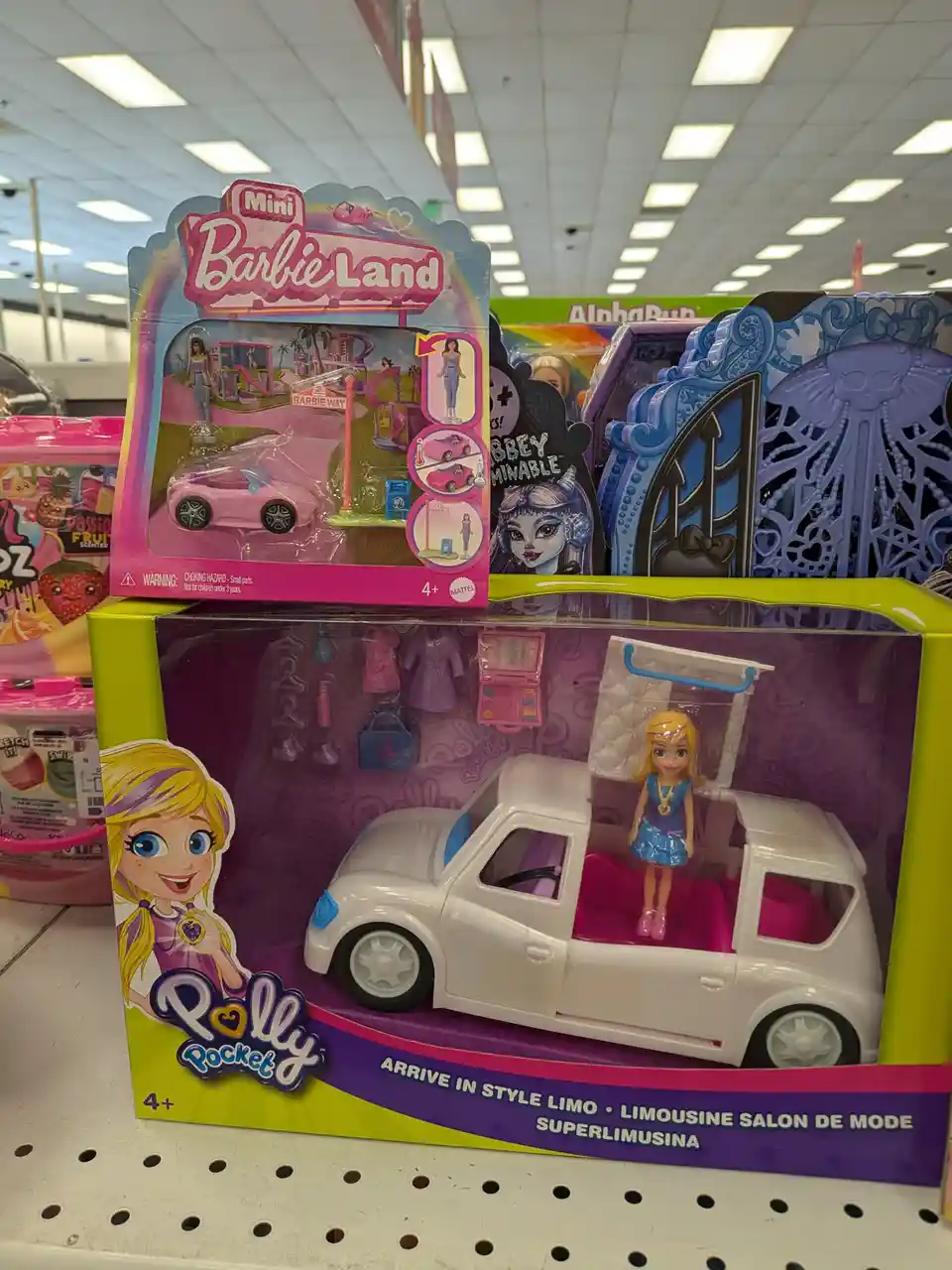 A photo of two toy sets on a store shelf: a 'Mini Barbie Land' set with a pink car and a 'Polly Pocket' set with a white…