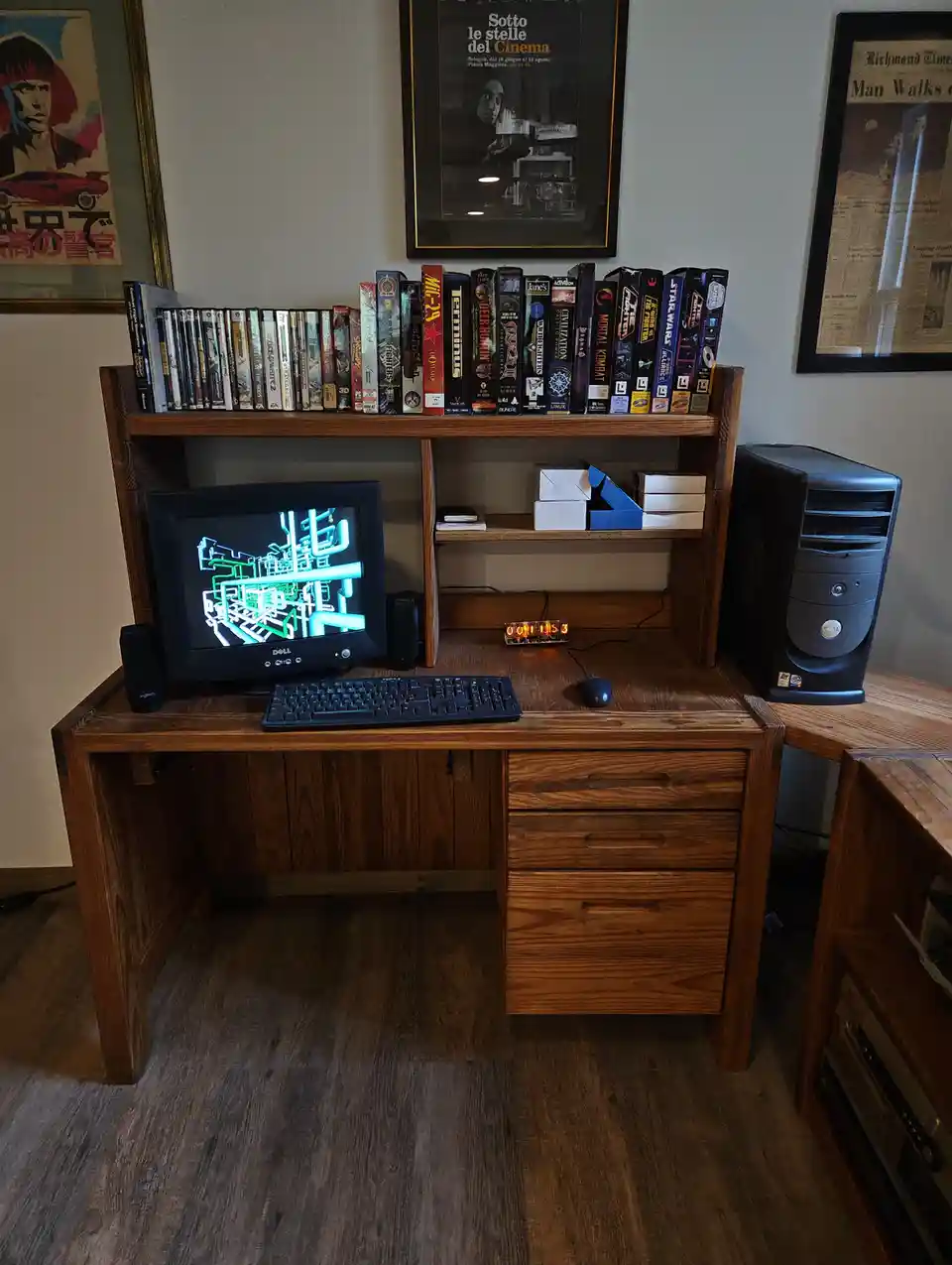 A wooden desk setup with a Dell CRT monitor displaying a green wireframe game, a keyboard, mouse, and a black computer…