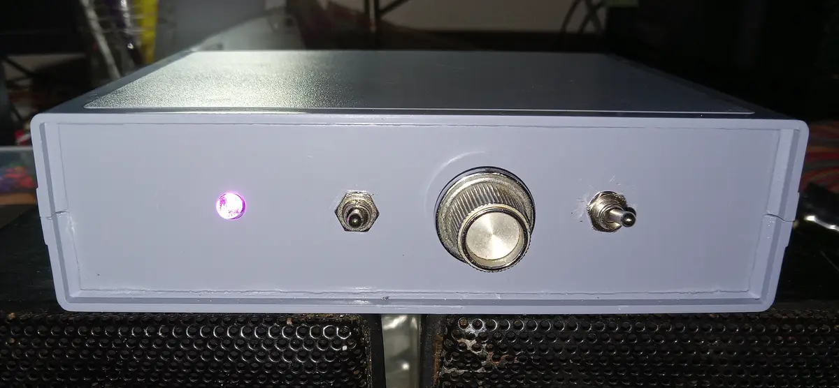 A close-up photo of a gray electronic device with a glowing purple LED light, a large central knob, and two smaller…