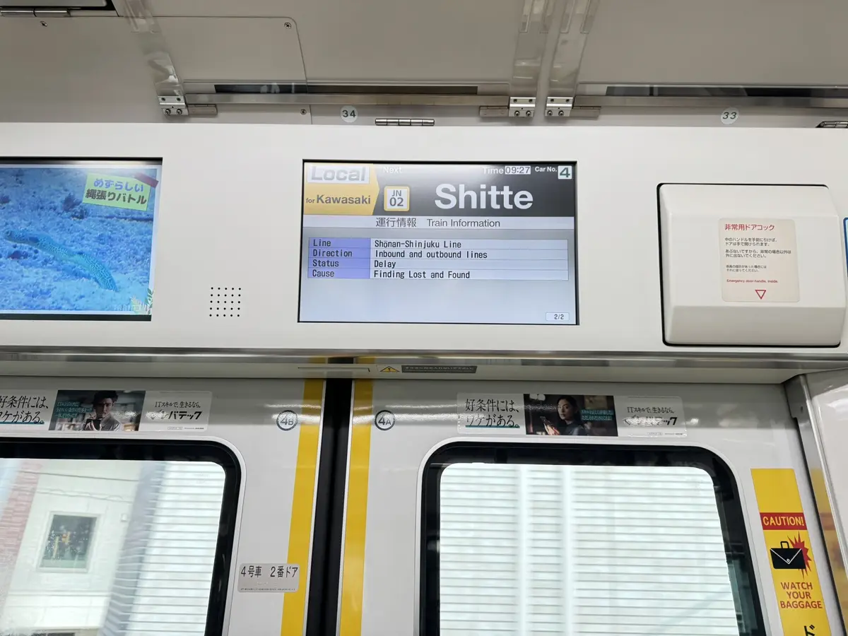 A photo of a train's digital display inside a Japanese train car, showing a train status screen with the next stop listed as…