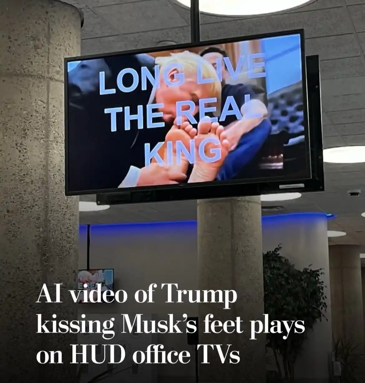 A large office TV screen displays an AI-generated video of Donald Trump kissing Elon Musk's feet, overlaid with the text…