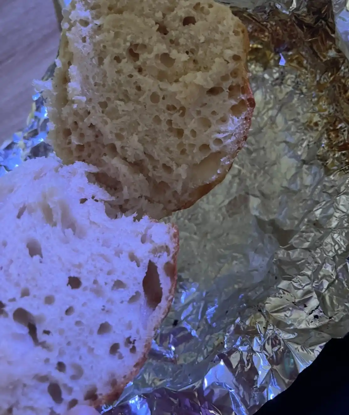 A close-up photo shows two halves of a freshly baked bread roll, revealing a soft, airy crumb texture with numerous holes…