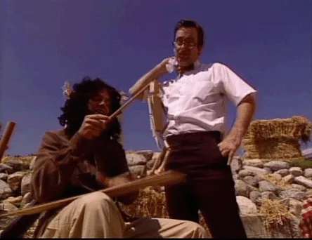 A split-screen image shows two identical frames of a man in a white shirt and dark pants standing behind another man seated…