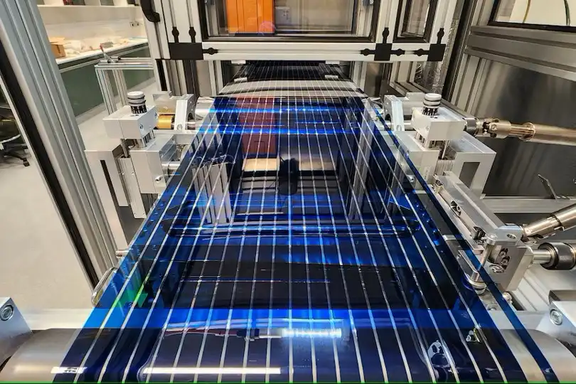 a blue solar panel with white grid lines is being transported on a conveyor belt through a factory machine. The panel is…